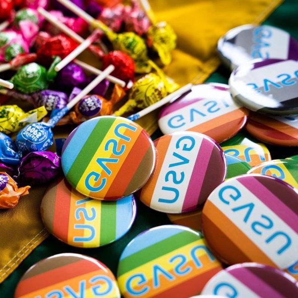 Buttons with various pride flags sit in a pile. They all read GVSU.