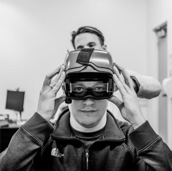 Justen Knape, a graduate student, dons immersive headset in the community hearing clinic with the help of Colton Clayton standing behind him